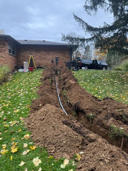 Trenched yard beside brick house, with exposed pipes and piles of dirt along a dug path
