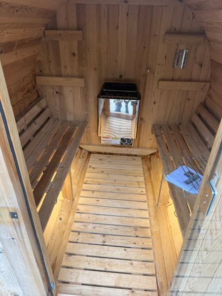 Wood-paneled sauna with two benches, a central heater, and warm lighting