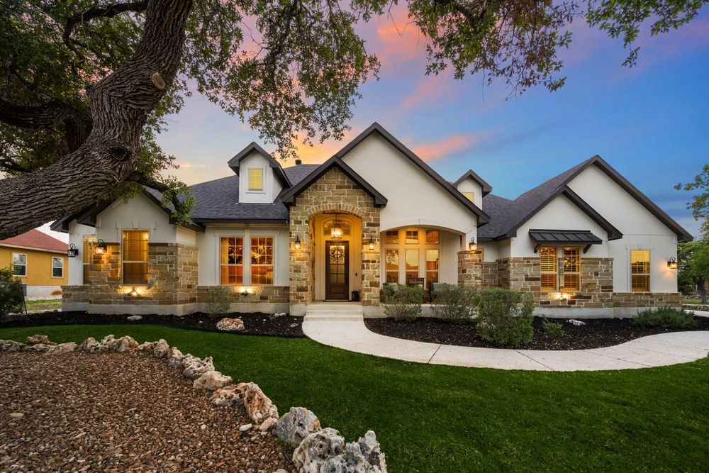A sprawling single-story house with a stone facade, stucco walls, and dark roof during a colorful twilight sunset.