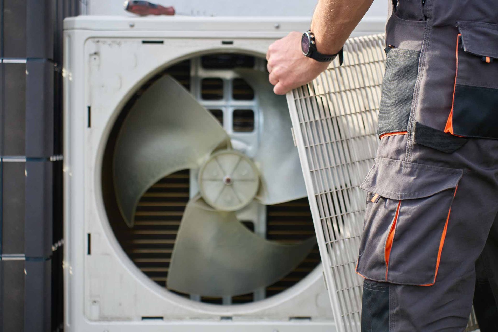 HVAC technician removing fan grille cover during outdoor AC condenser unit maintenance and repair. HVAC technician removing fan grille cover during outdoor AC condenser unit maintenance and repair.