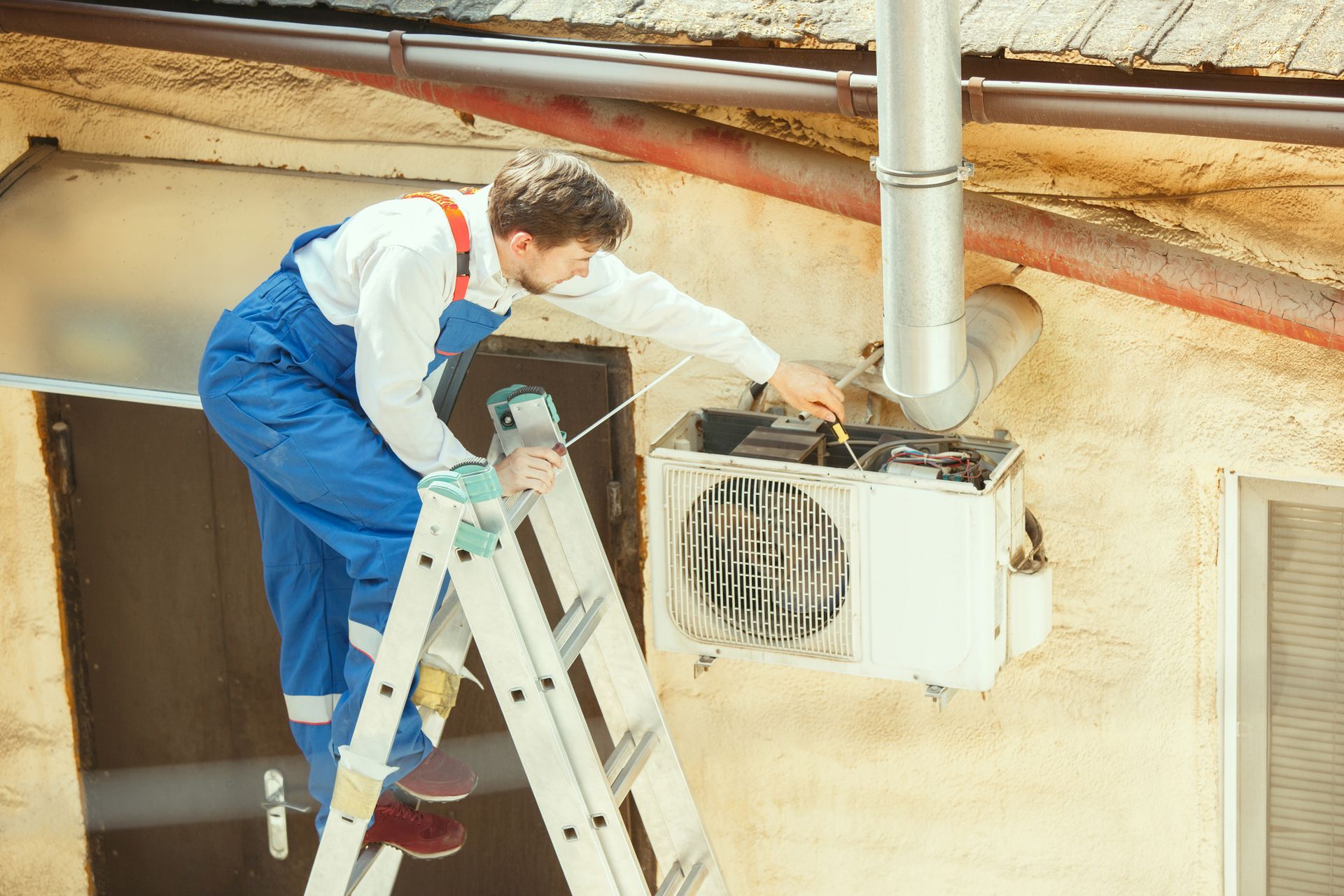 Technician repairing outdoor air conditioner unit on ladder during HVAC maintenance.