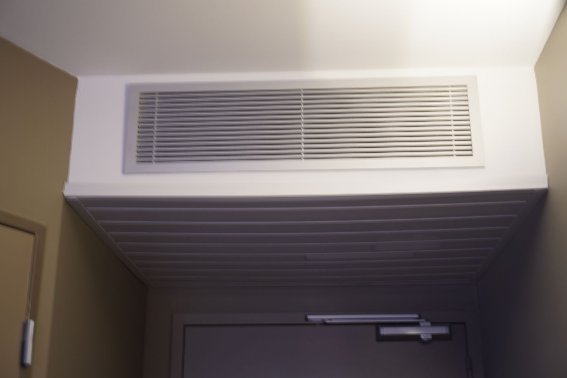 Interior ceiling view of a modern ductless AC unit above a door in a residential hallway.