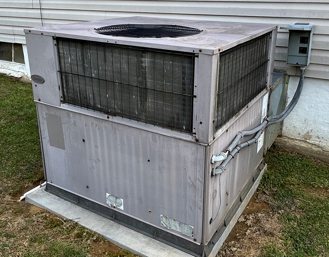 Large gray rooftop HVAC unit beside a building wall with vents and wiring.