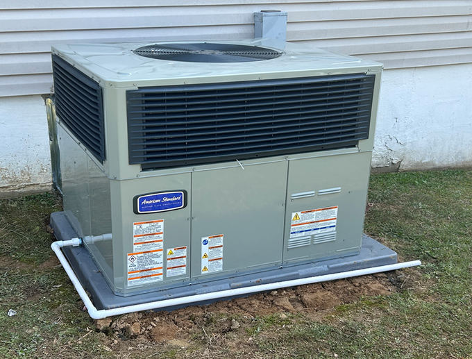 Large gray HVAC unit outdoors beside a house wall, with dark vents on top and sides.