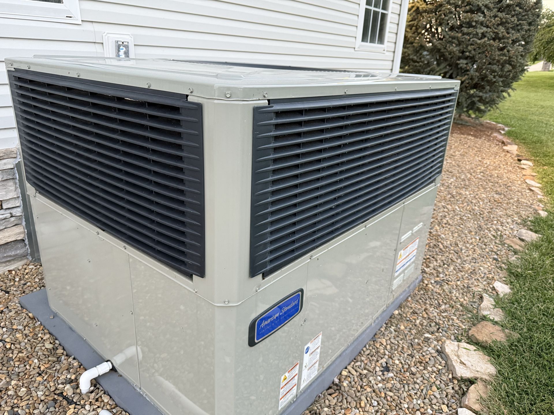 Exterior air conditioning unit next to a house with dark gray vents.