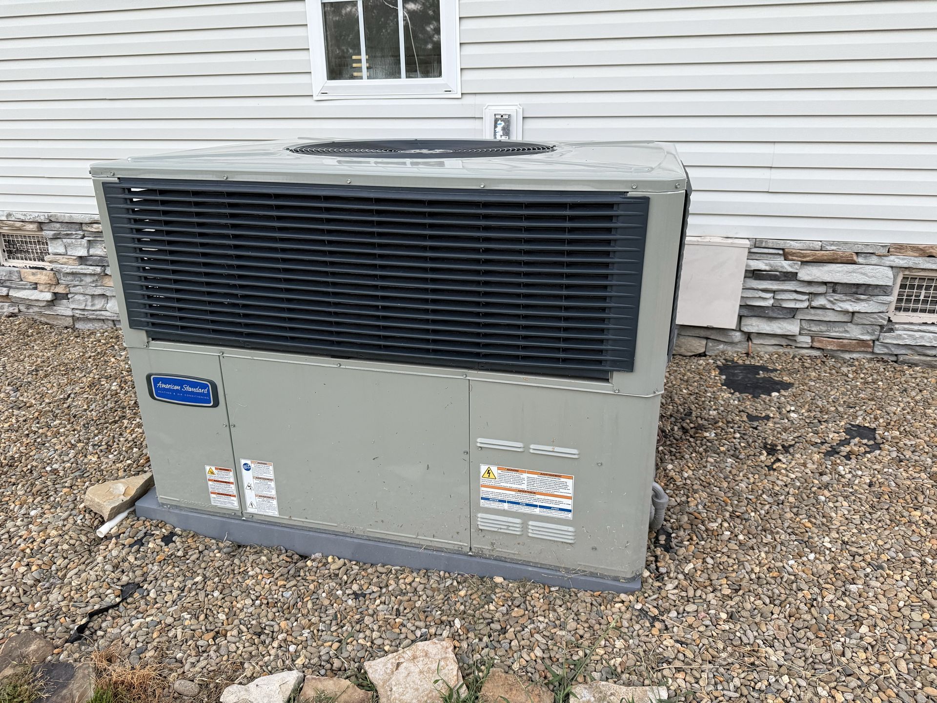 Gray air conditioning unit outside a building with white siding and gravel.