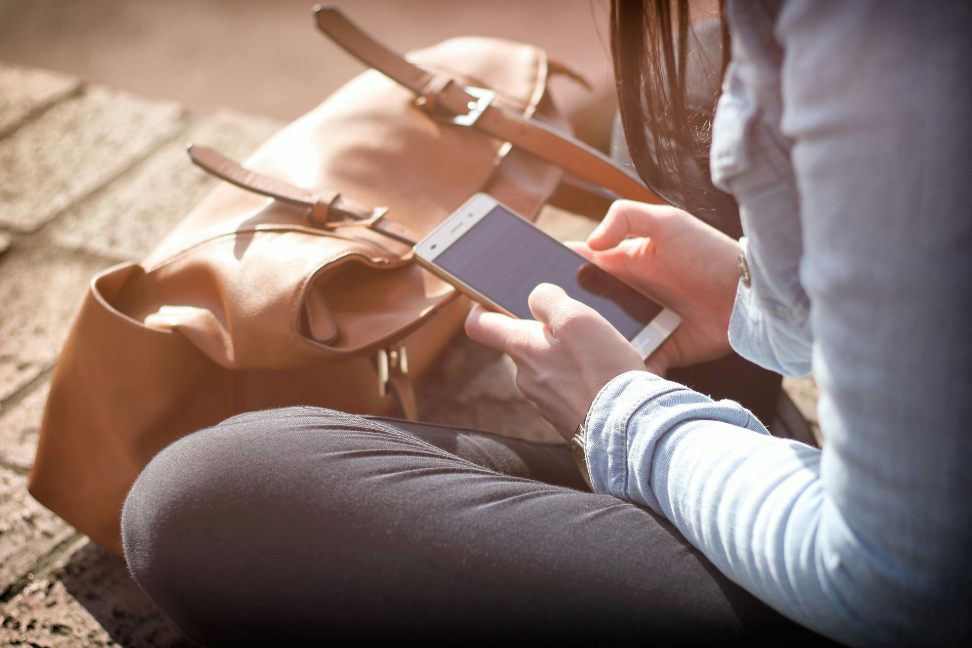 A woman is sitting on the ground using a cell phone.