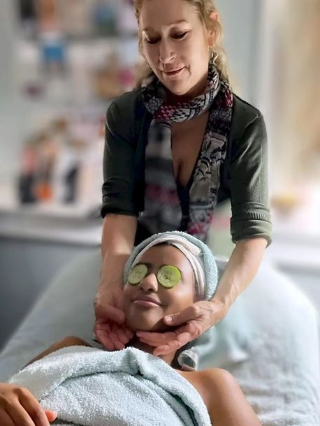 A woman is giving a woman a massage with cucumber slices on her eyes.