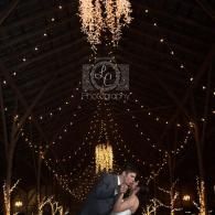 Couple embracing under warm string lights in a dark, decorated hall