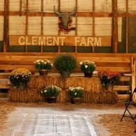 Rustic farm venue with hay bales, flower arrangements, and a “CLEMENT FARM” sign on a wooden wall