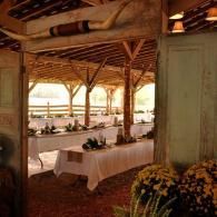 Long banquet tables under a rustic wooden pavilion with white tablecloths and floral centerpieces