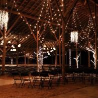 String-lit rustic event hall with wooden beams and folding chairs at round tables
