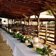 Wooden barn aisle with white-draped tables and green plants under a rustic roof