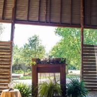 Rustic open-air venue with wooden beams, a decorated altar, and greenery outside