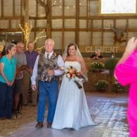 Bride and man walking down aisle in a rustic barn wedding venue, guests watching nearby