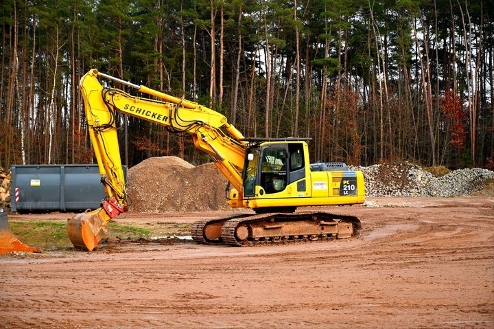 A yellow Komatsu excavator parked on a dirt construction site with a forest in the background.