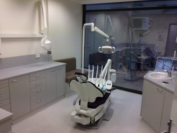 Dental office with dental chair, cabinets, and equipment. A window provides outside view.