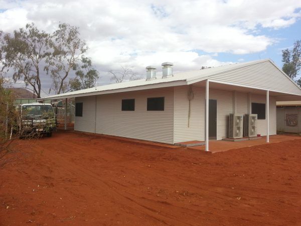 White building with a covered porch, air conditioning units, and red dirt in an outdoor setting.
