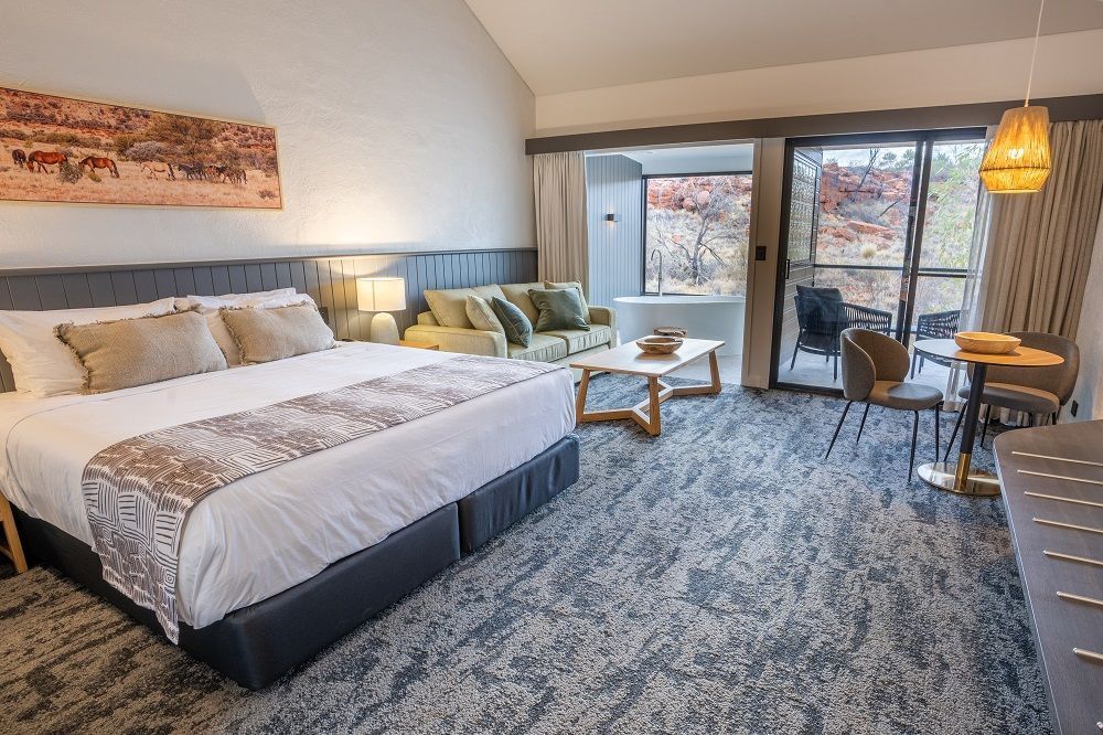 Hotel room with king bed, sofa, table, balcony overlooking red rocks.