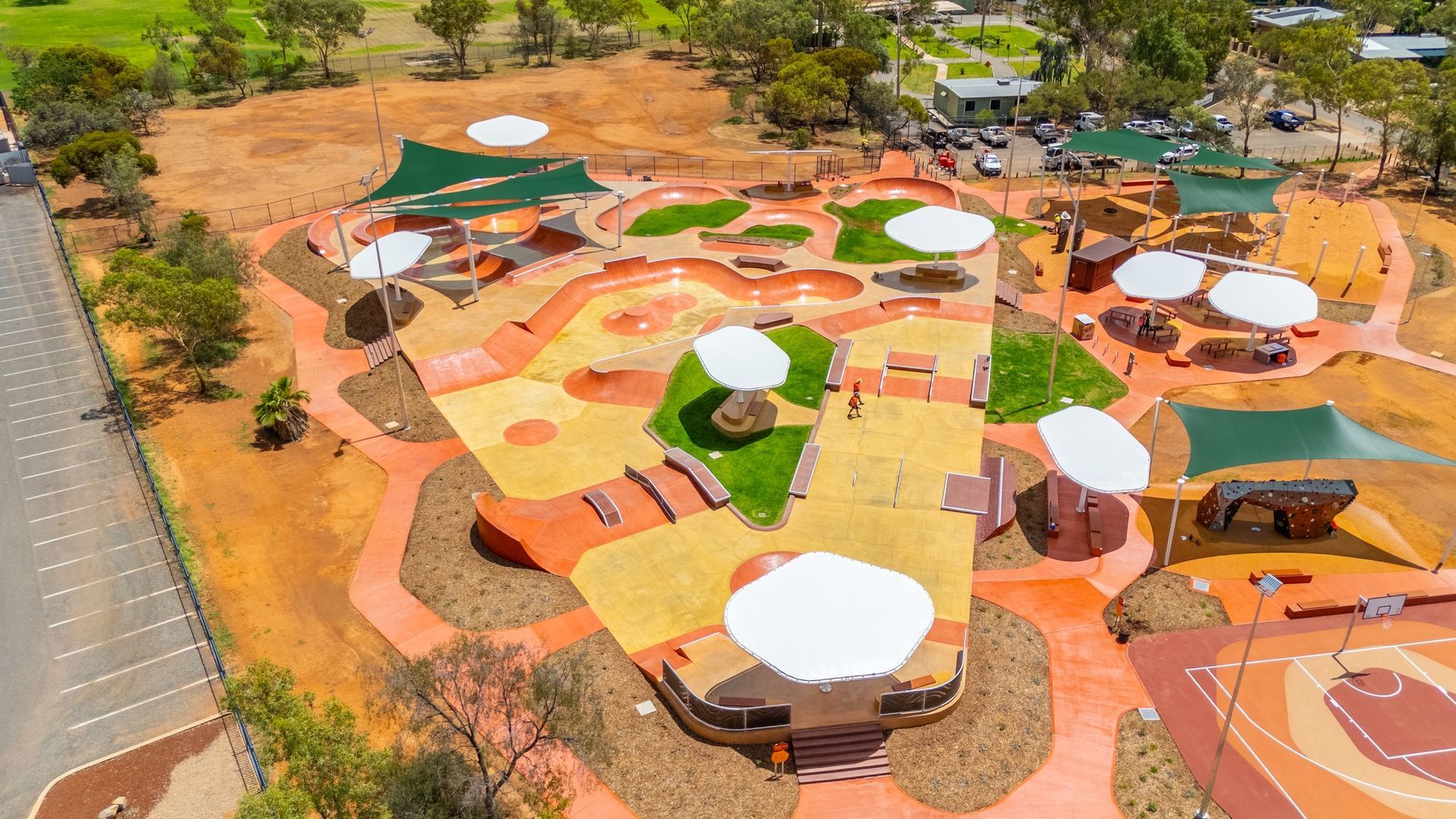 Aerial view of a brightly colored outdoor playground with shaded seating areas and a basketball court.