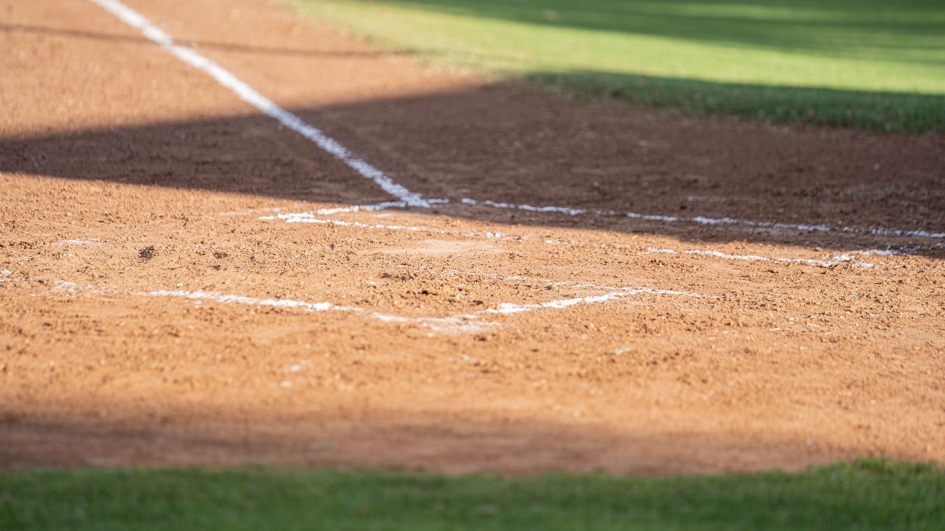 Home plate and white foul lines marked on a dirt baseball field, with grass bordering the edges.