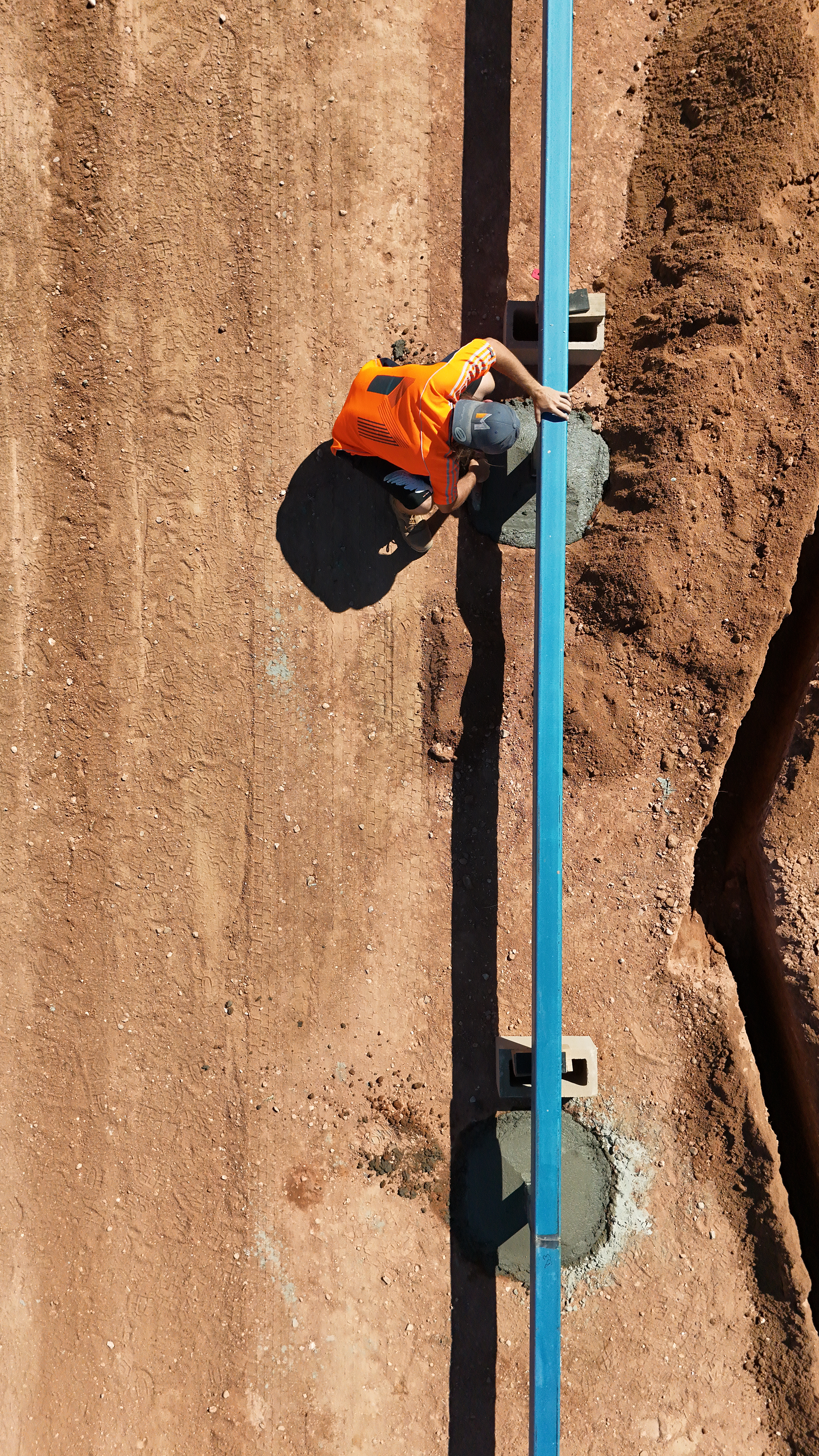 Worker in orange vest climbing a blue ladder on a dirt wall with harness gear