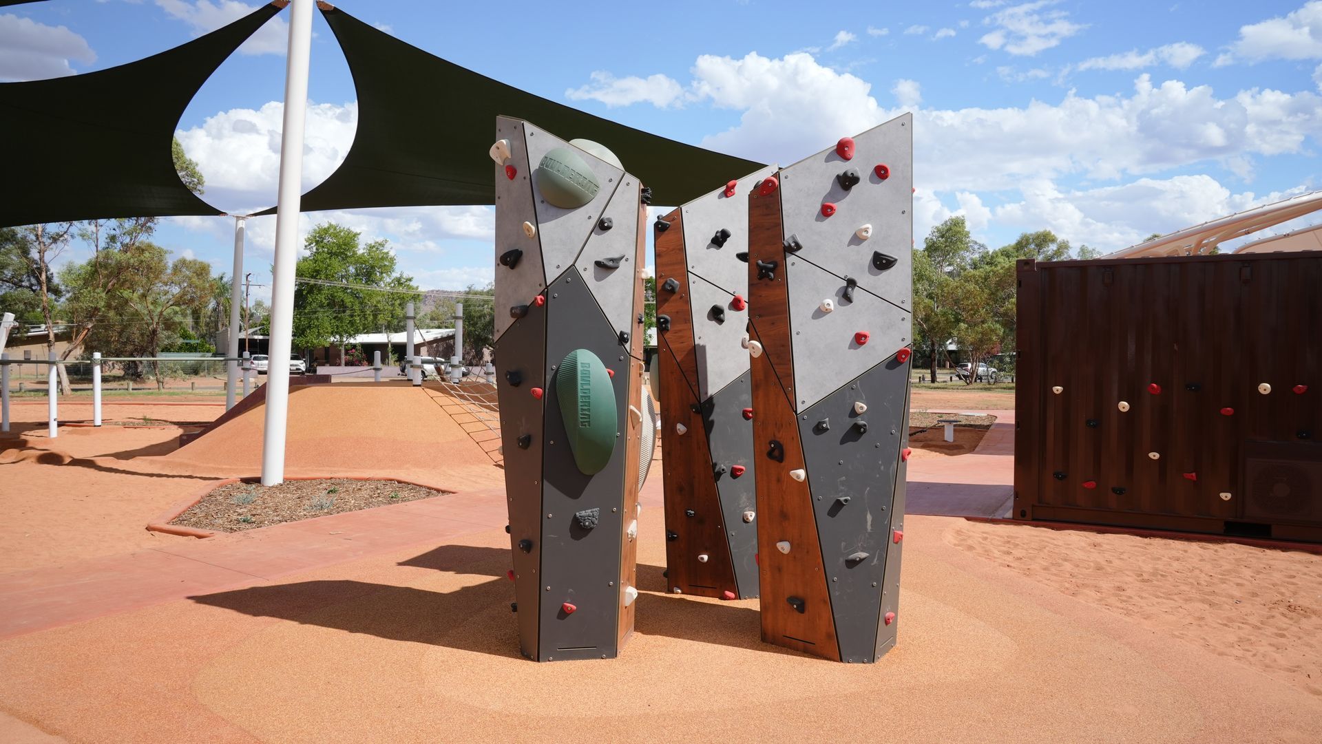 Climbing wall in a park with colorful holds. Shade structure overhead.