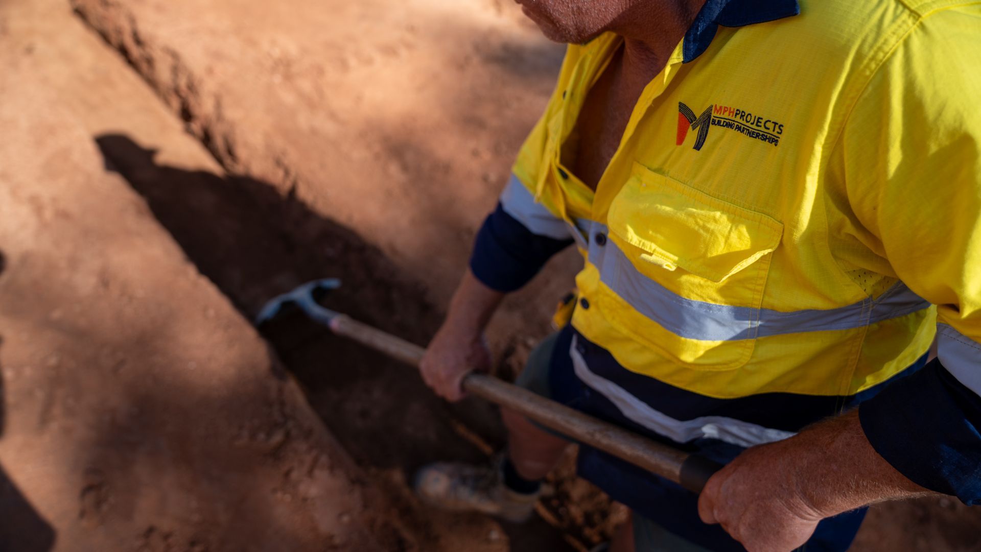 Person in yellow work shirt digging in dirt with a shovel in Alice Springs