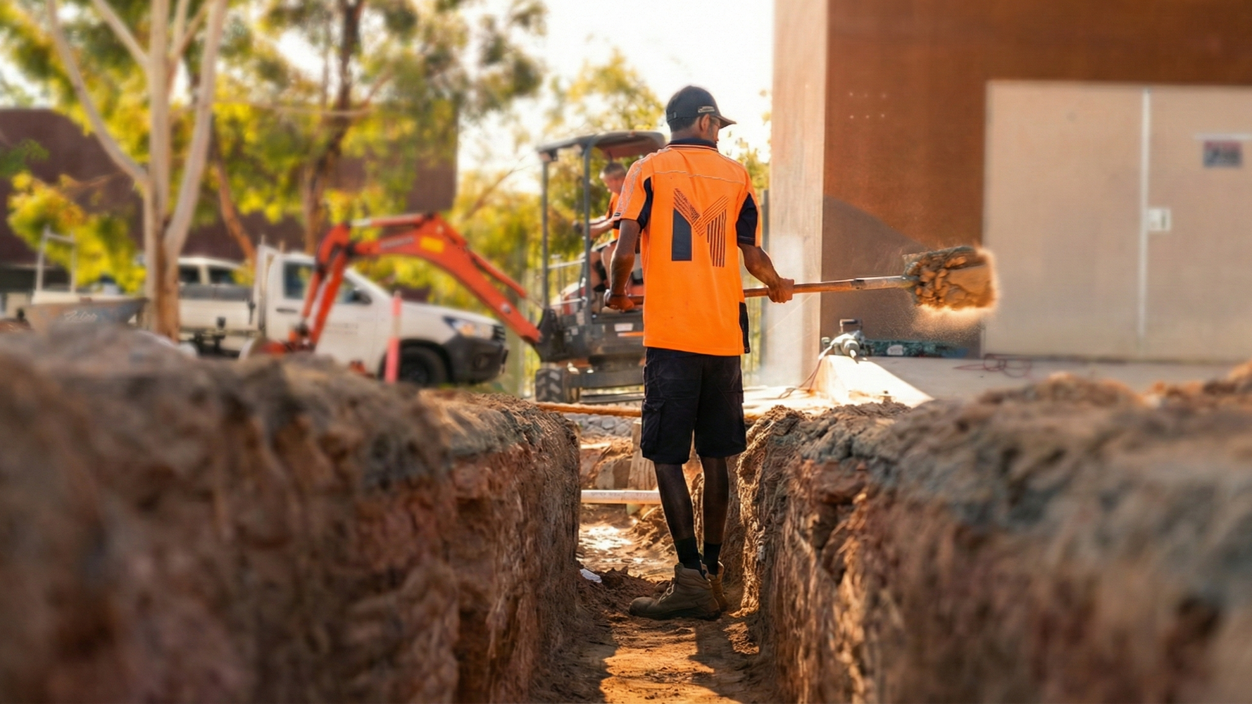 Worker in an orange safety vest digging a trench at a construction site.