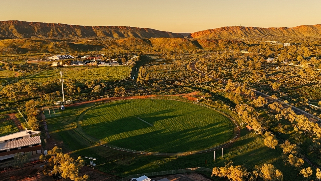 Aerial view of a green sports field in a valley beside hillside neighborhoods at sunset
