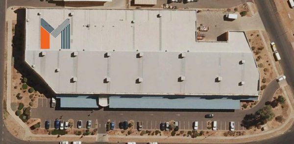 Aerial view of a large warehouse with a large M logo on the roof, parking lot in front.