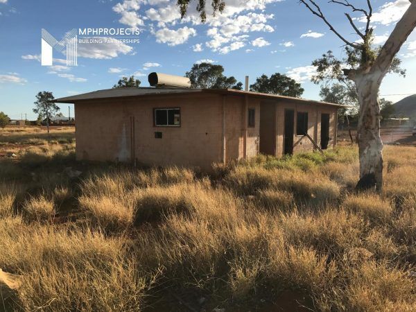 A weathered, single-story building sits in tall, dry grass, under a cloudy sky.