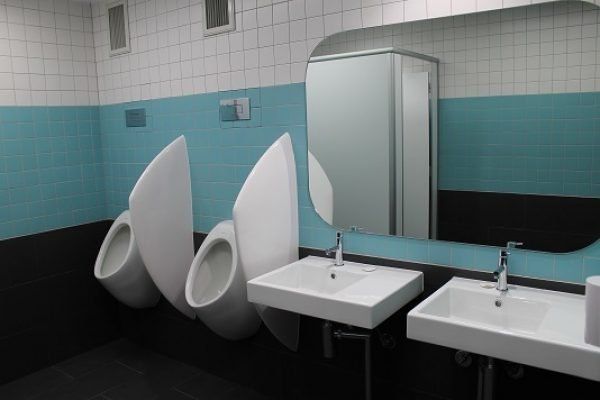 Modern public restroom with three white urinals and two sinks; turquoise and black walls.