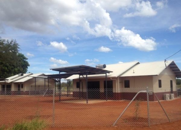 Houses with solar panels under a blue sky, behind a chain-link fence.