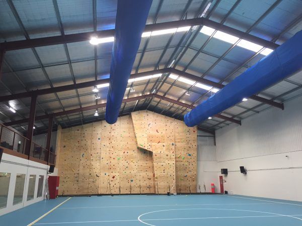 Indoor climbing wall with blue floor and ceiling, red and white wall holds.