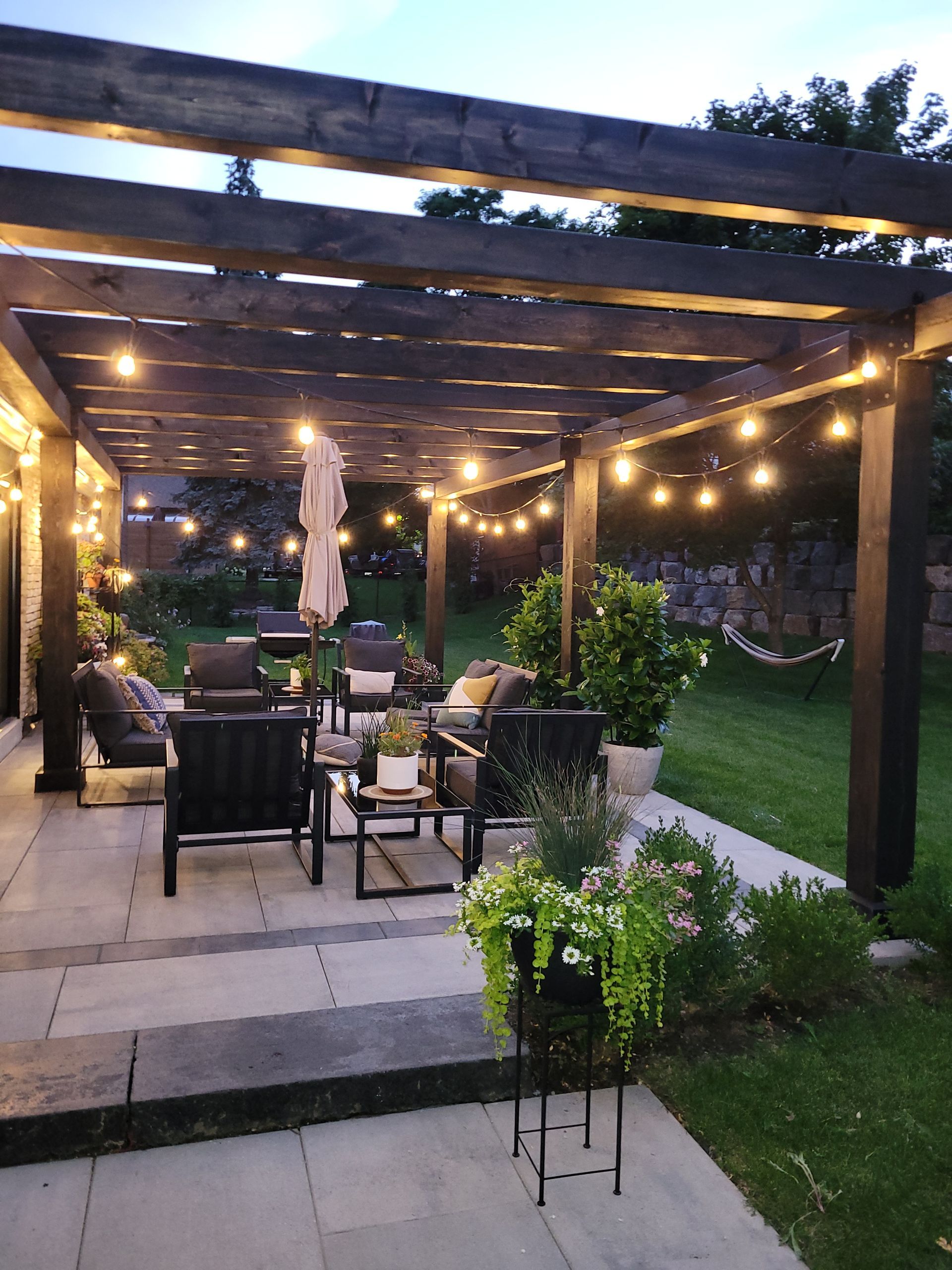 Patio with pergola, string lights, and outdoor furniture. Green lawn in background.