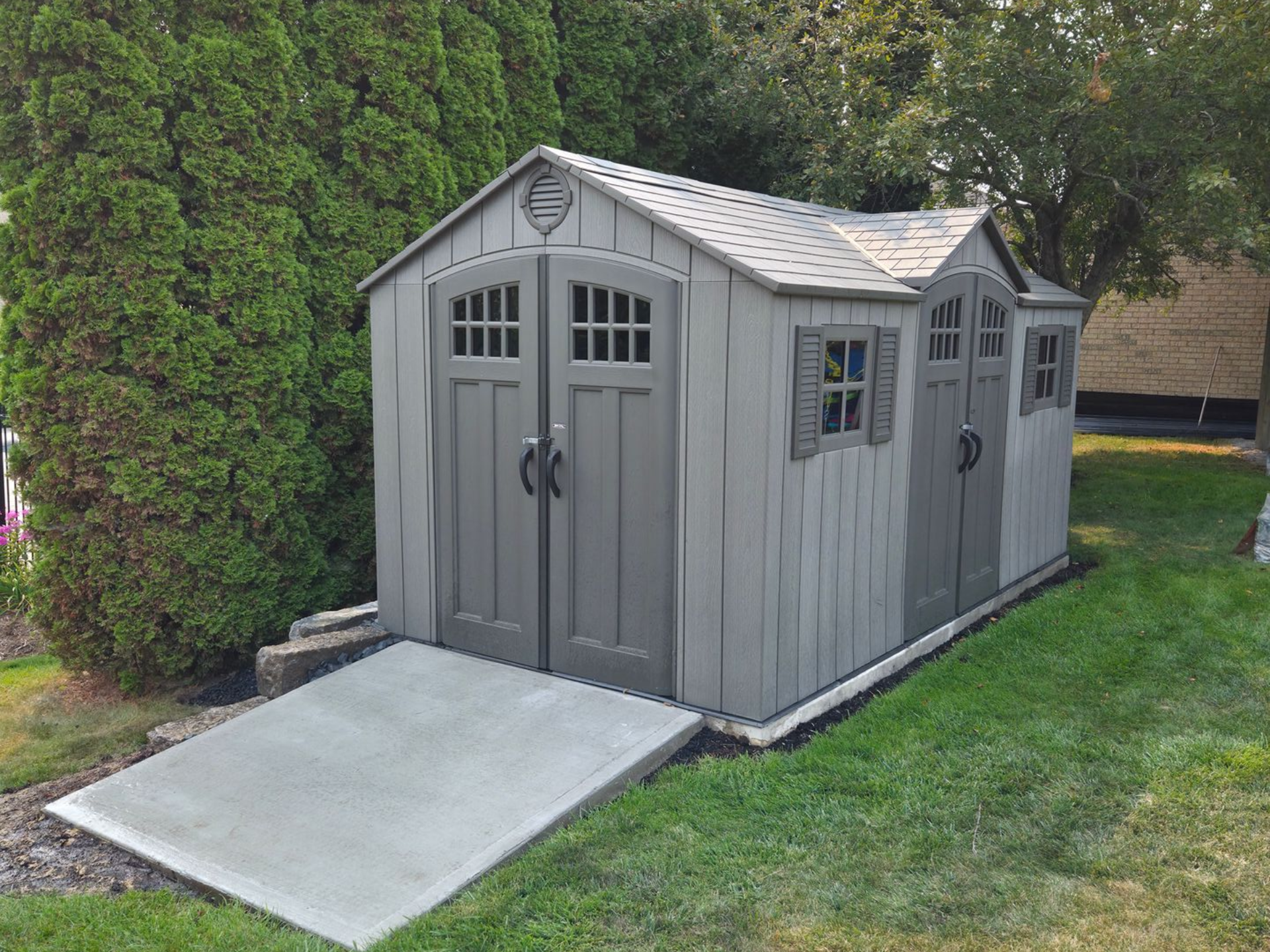 Gray storage shed with concrete ramp in a yard.