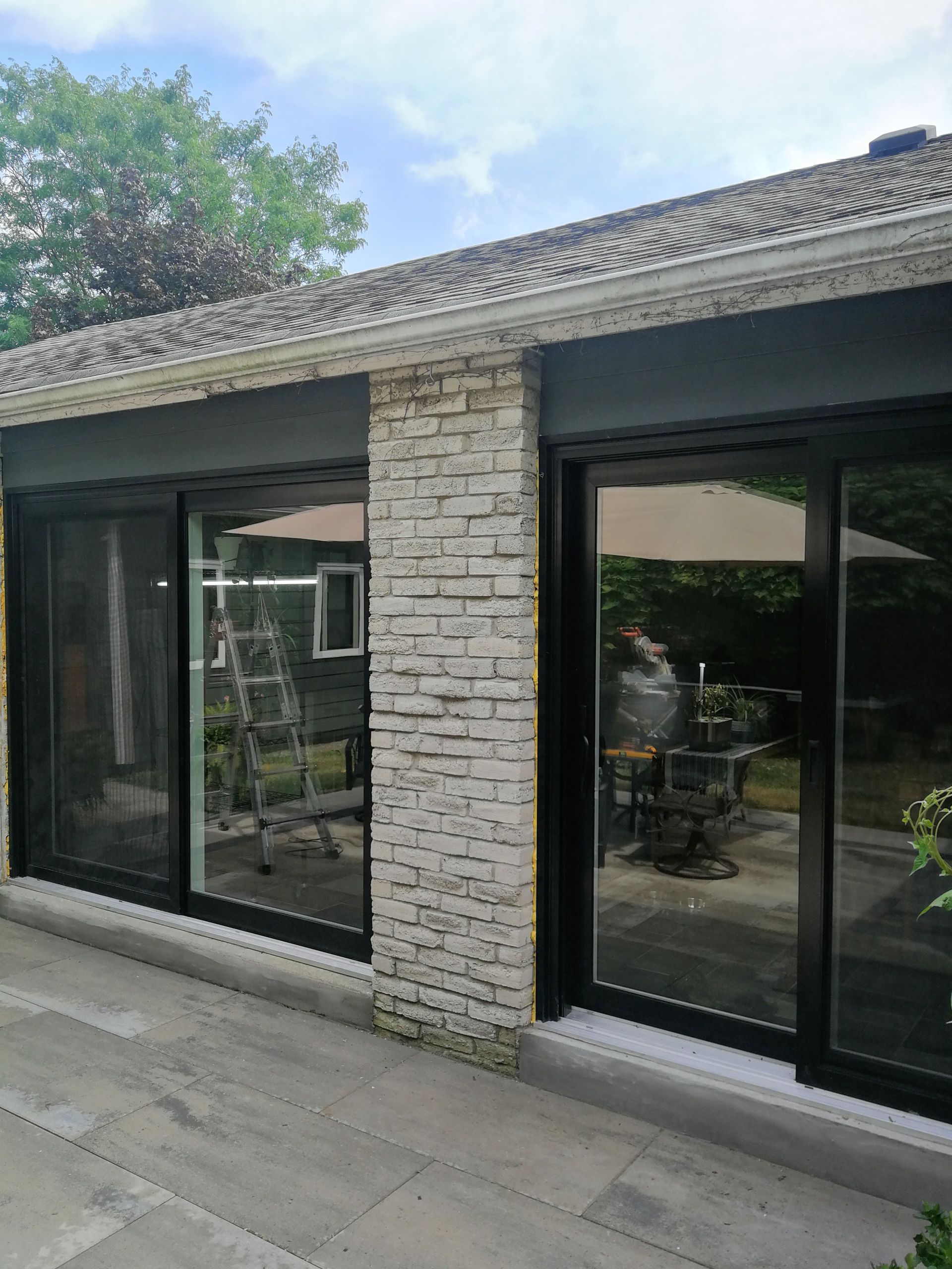 Sliding glass doors with black frames, set in a stone wall, reflecting outdoor patio and garden.