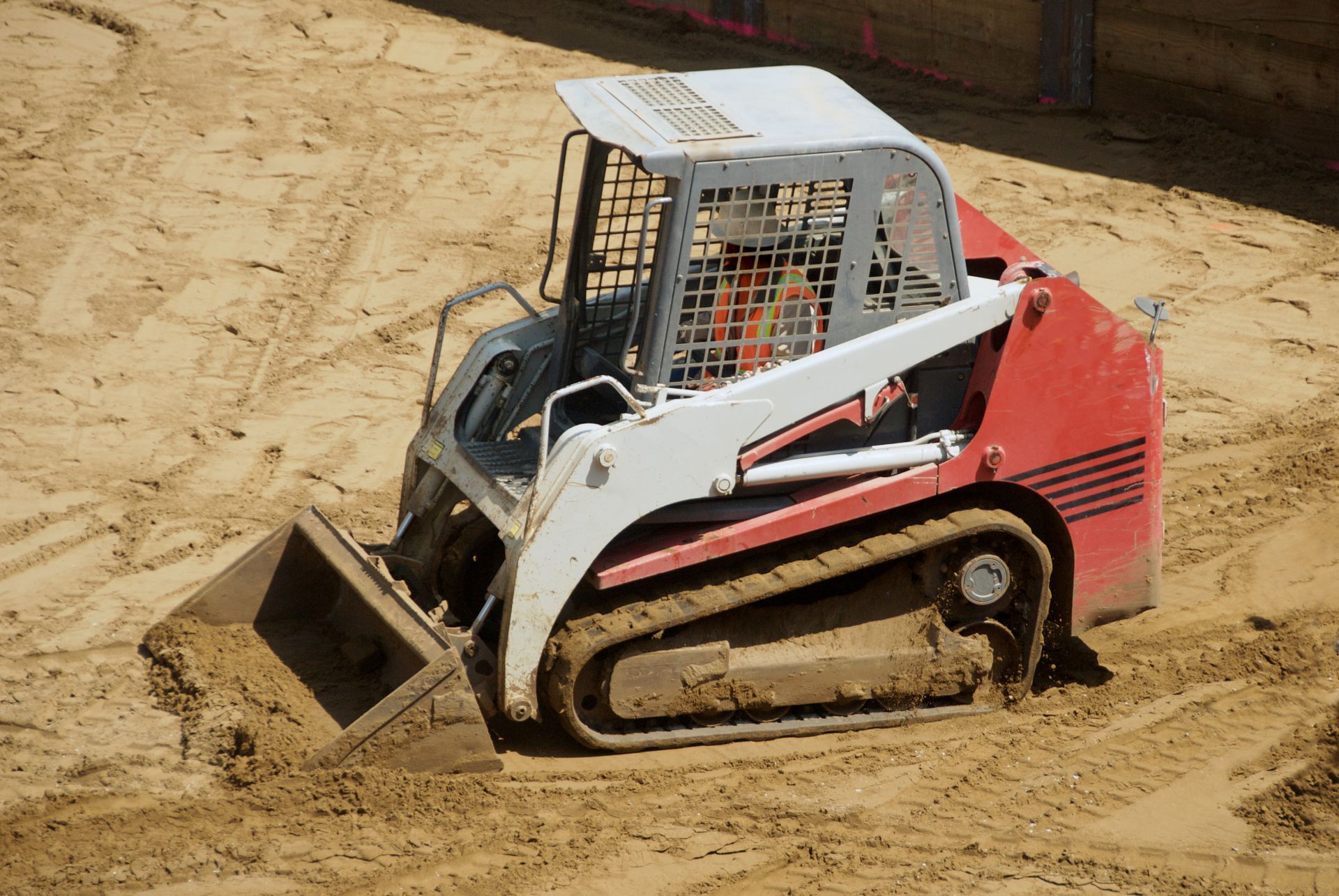 Red and white skid-steer loader pushing dirt on a sandy construction site