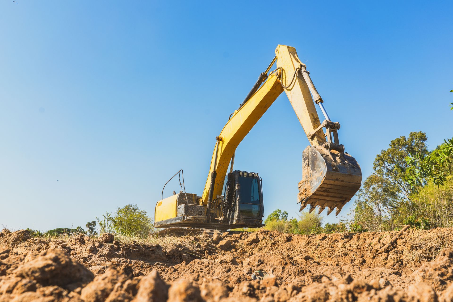 Yellow excavator digging dirt under a clear blue sky in a construction site
