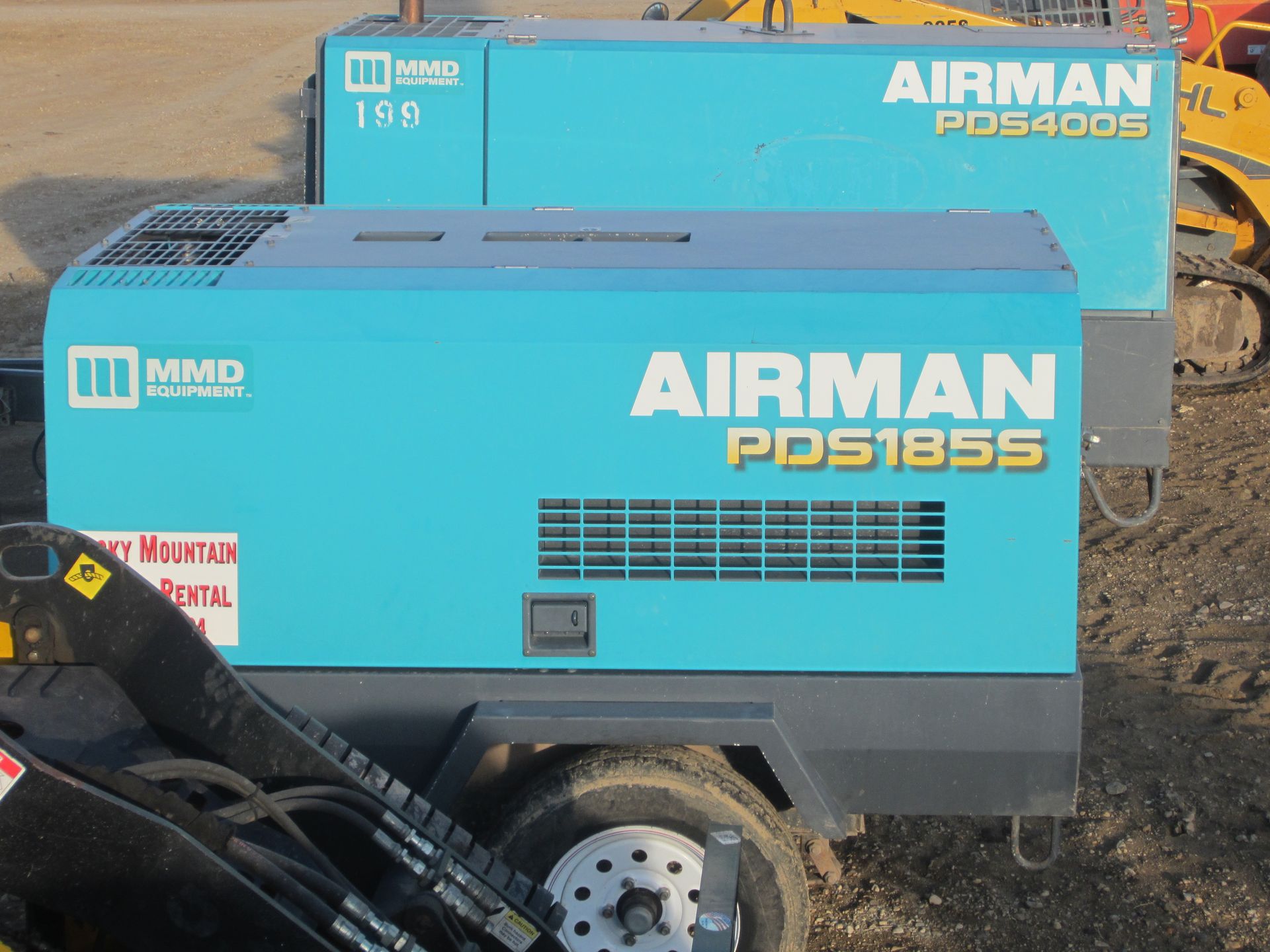 Blue AIRMAN portable air compressors on a trailer, with one labeled PDS185S in front and another behind.