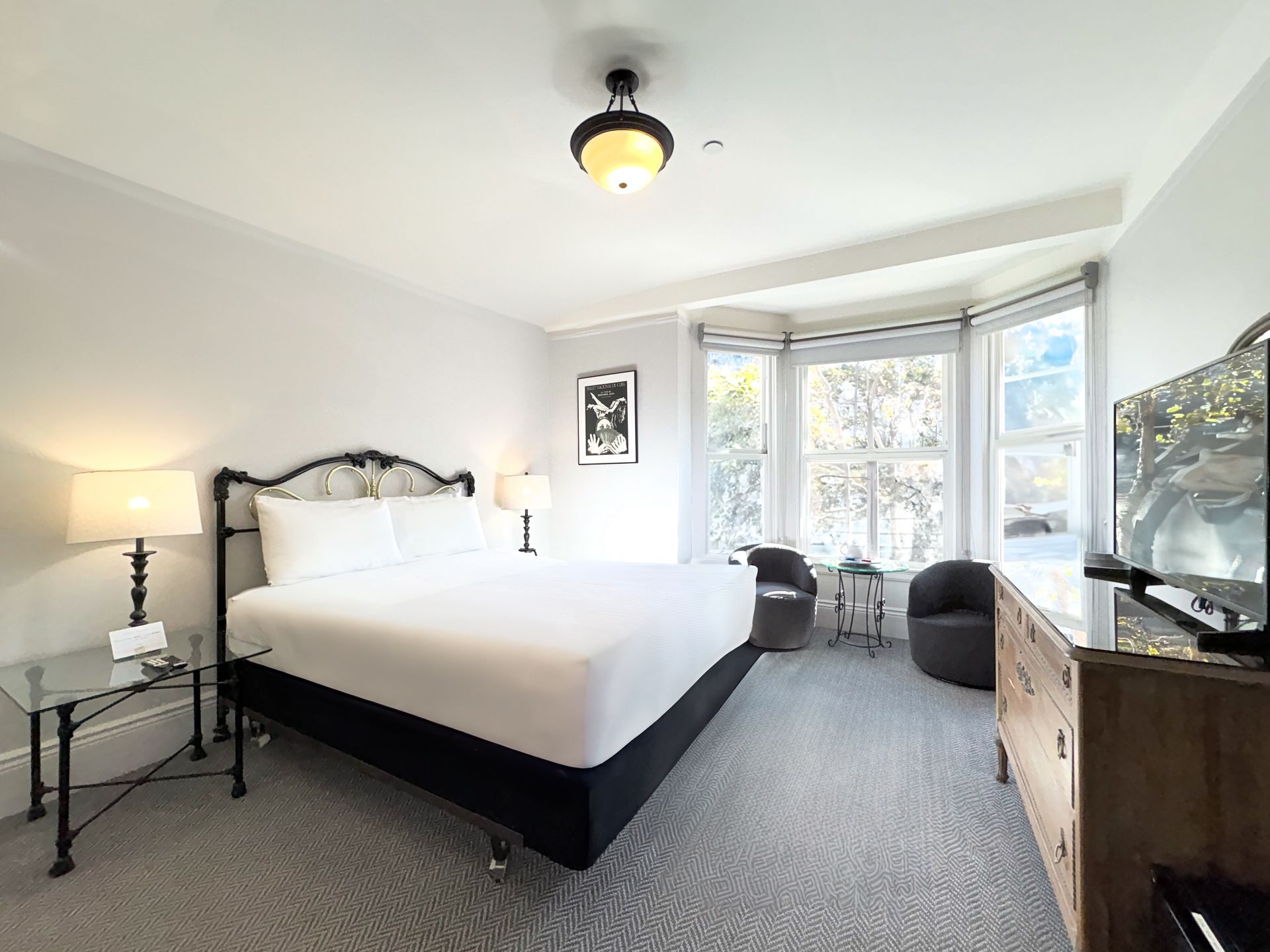 A hotel room with a king size bed , dresser , chairs and television.