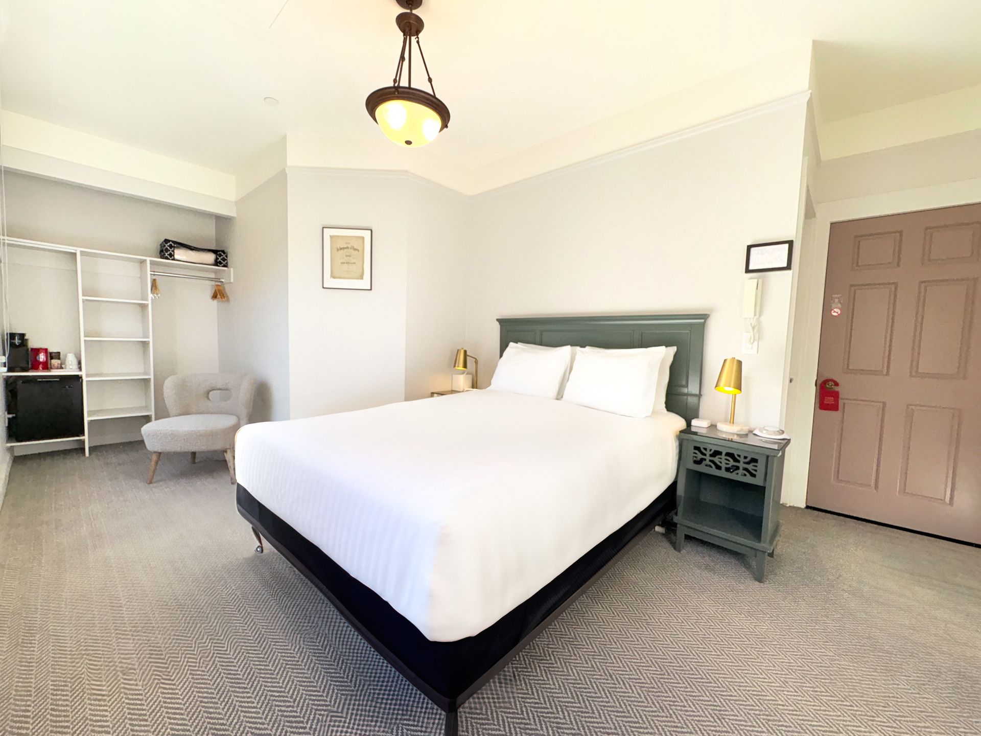 A hotel room with a bed , nightstand , chair and door.