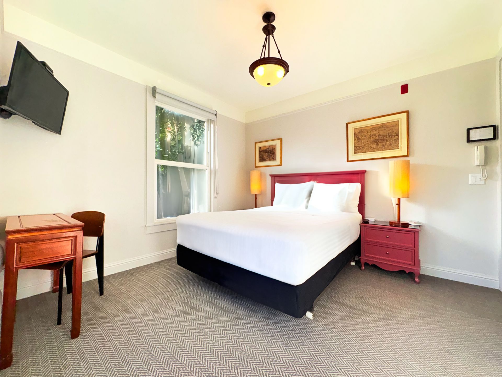 A hotel room with a king size bed , desk , nightstand and television.