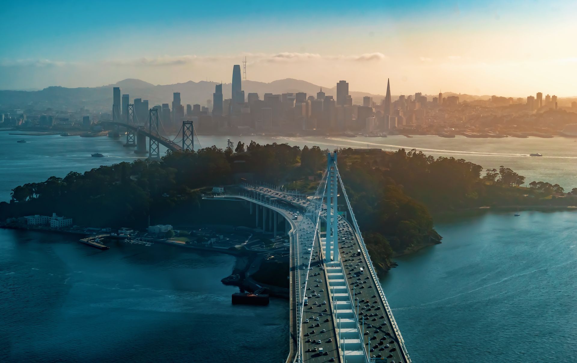 An aerial view of a bridge over a body of water with a city skyline in the background.
