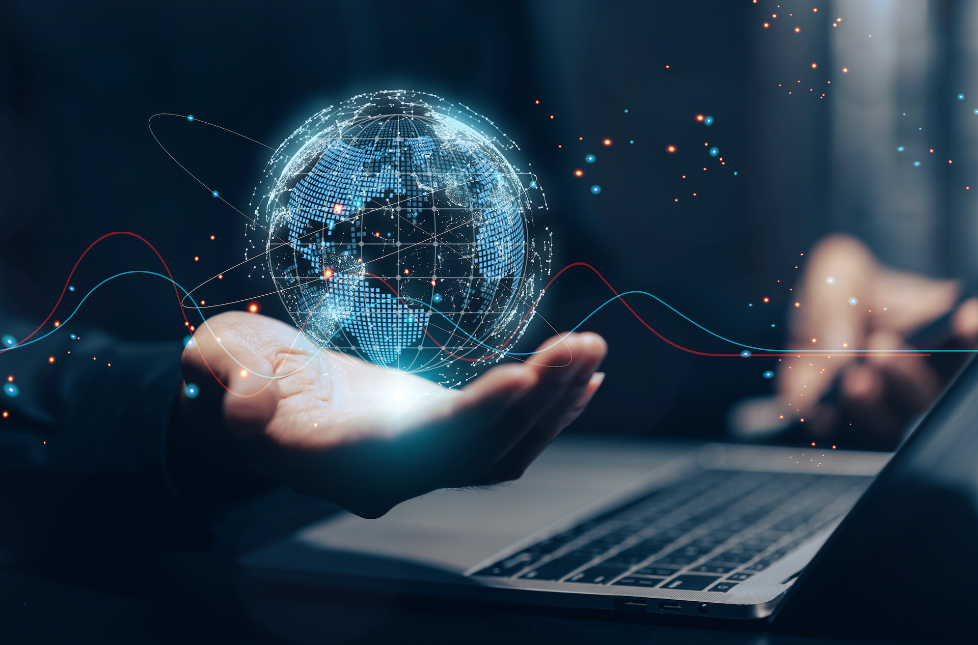 A person's hand holding a glowing digital globe above a laptop, representing data and technology.