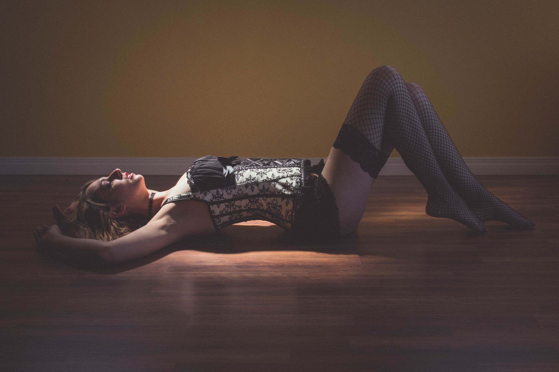 Beautiful woman in tasteful lingerie posing by laying on floor in spotlight of sunshine