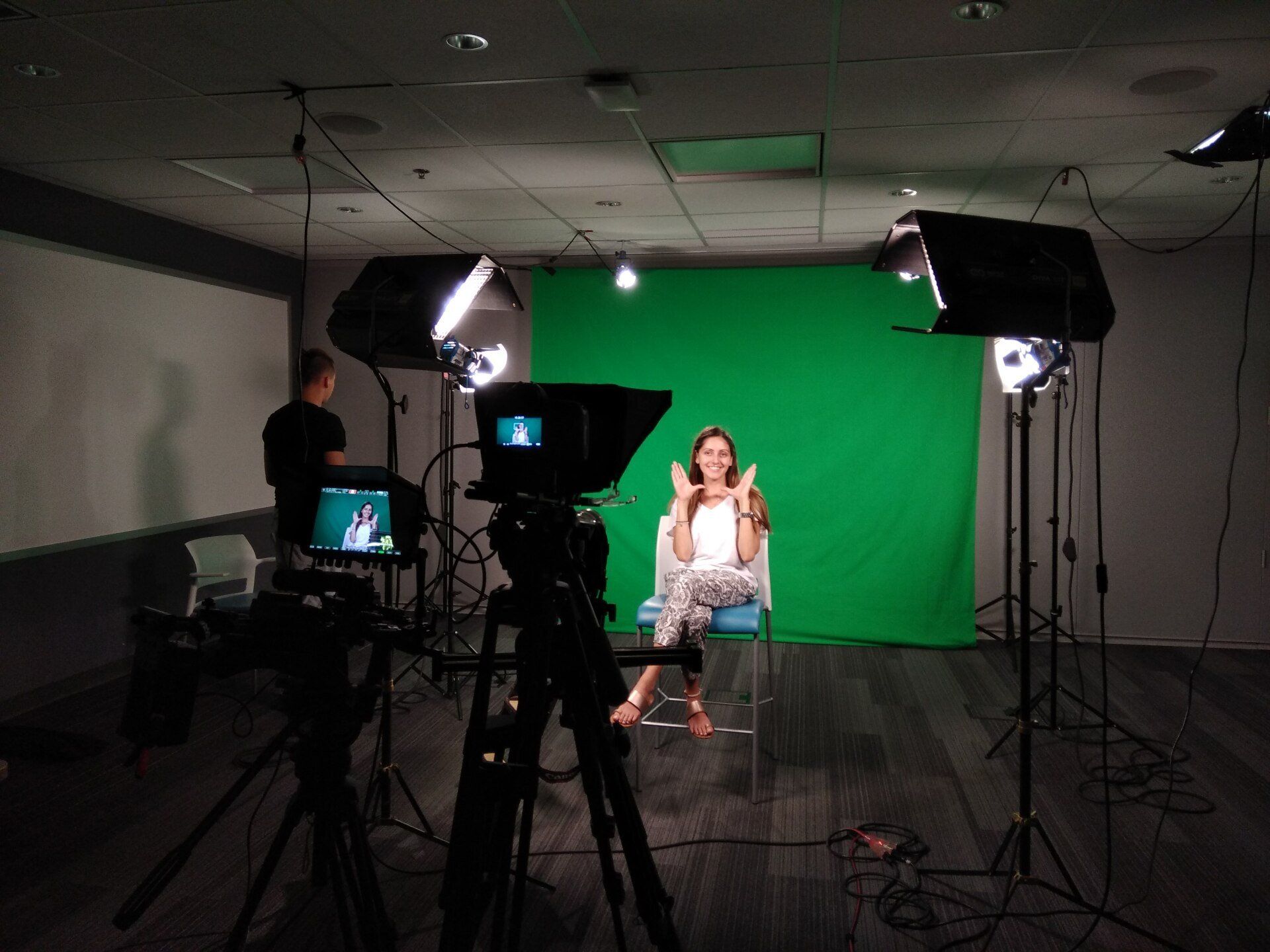 A woman is sitting in front of a green screen