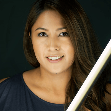 A woman in a blue shirt is smiling with a light behind her