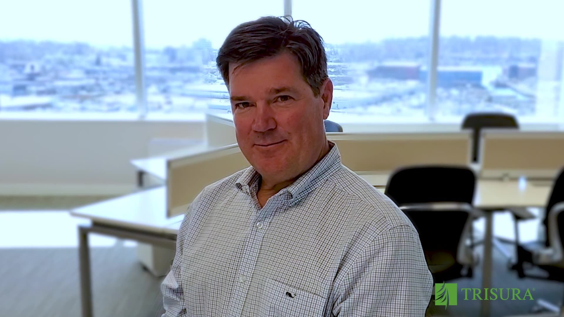 Man in patterned shirt smiling in a bright office with snowy city view through windows